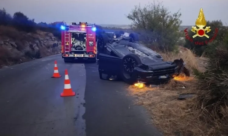 Auto ribaltata su una strada di campagna al crepuscolo, con mezzo dei vigili del fuoco, coni segnaletici e luci blu accese