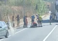 Un ciclista a terra soccorso da altri ciclisti e passanti lungo una strada provinciale, con auto e mezzo pesante in transito.