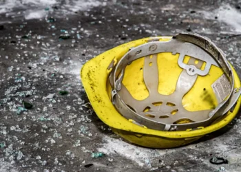 Casco giallo da cantiere appoggiato a terra tra vetri infranti e detriti
