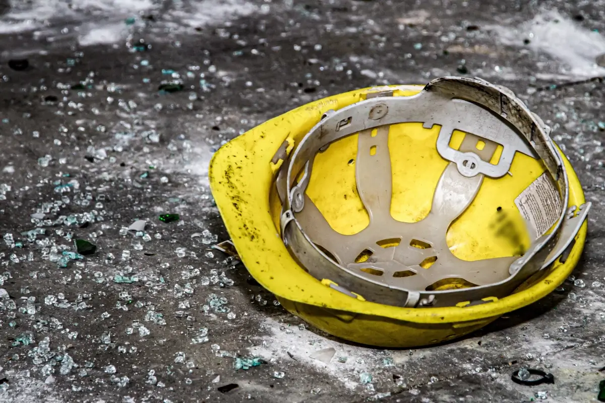 Casco giallo da cantiere appoggiato a terra tra vetri infranti e detriti