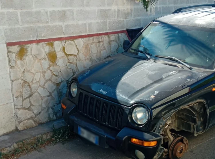Auto fuoristrada danneggiata con ruota anteriore mancante, ferma vicino a un muro di pietra a Scoglitti