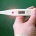 Mano che regge un termometro digitale con 38,75 gradi sul display, febbre alta tipica dei sintomi dell'influenza