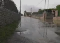 Strada allagata in via Pluchino a Modica: acqua piovana ristagna tra muretti a secco sotto un cielo grigio