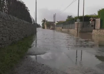 Strada allagata in via Pluchino a Modica: acqua piovana ristagna tra muretti a secco sotto un cielo grigio