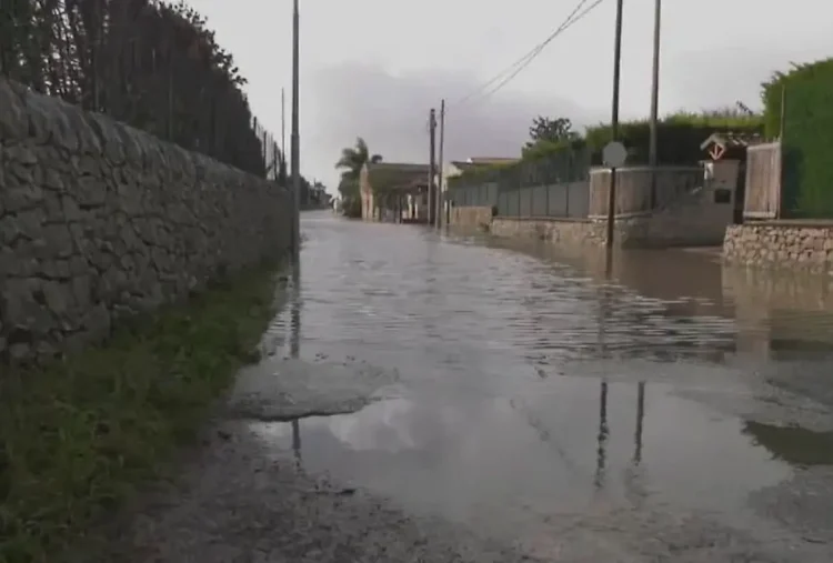 Strada allagata in via Pluchino a Modica: acqua piovana ristagna tra muretti a secco sotto un cielo grigio