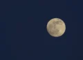 Luna piena quasi al completo nel cielo blu della sera, con i mari lunari scuri ben visibili sul disco