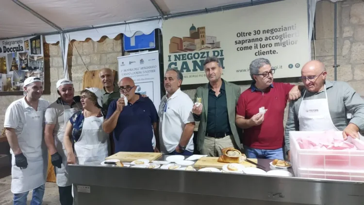 Gruppo di espositori assaggia prodotti da forno allo stand della mostra artigianale nel centro storico di Gangi.