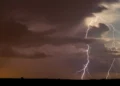 Maltempo: fulmini ramificati tra nubi scure sopra un'area di campagna piatta, con luce arancione all'orizzonte