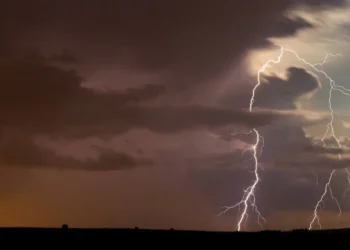 Maltempo: fulmini ramificati tra nubi scure sopra un'area di campagna piatta, con luce arancione all'orizzonte