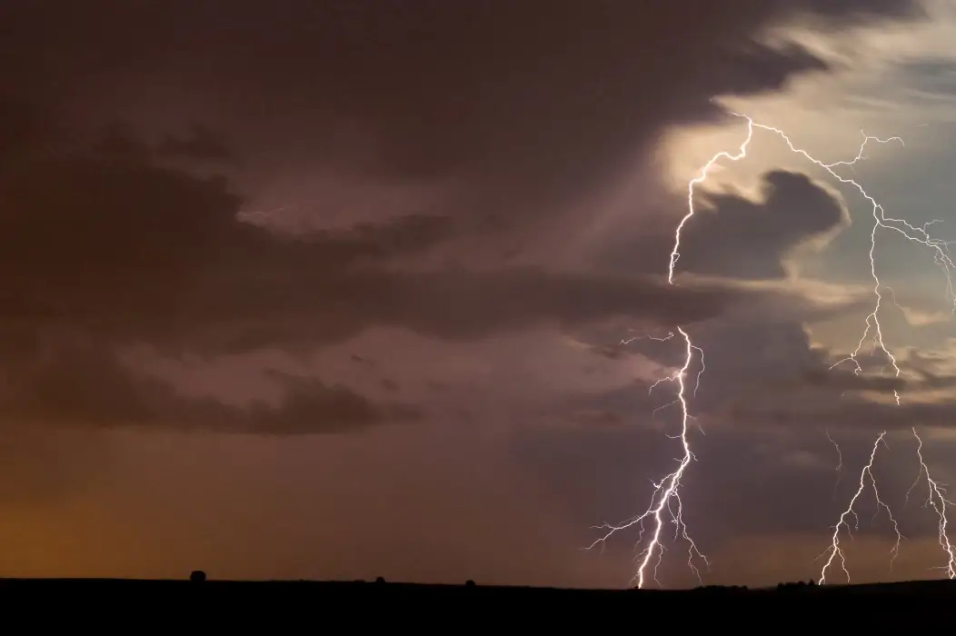 Maltempo: fulmini ramificati tra nubi scure sopra un'area di campagna piatta, con luce arancione all'orizzonte
