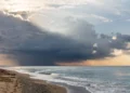 Nuvola temporalesca scura sul mare durante il maltempo, con raggi di sole tra le nubi e onde sulla spiaggia