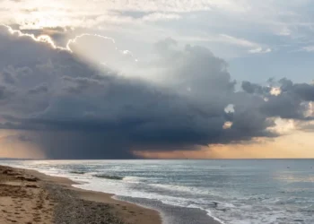 Nuvola temporalesca scura sul mare durante il maltempo, con raggi di sole tra le nubi e onde sulla spiaggia