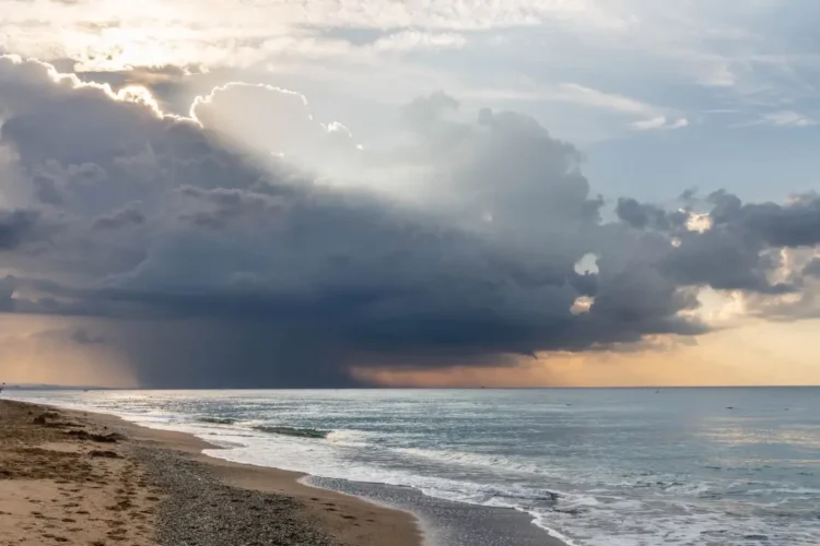 Nuvola temporalesca scura sul mare durante il maltempo, con raggi di sole tra le nubi e onde sulla spiaggia