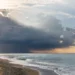 Nuvola temporalesca scura sul mare durante il maltempo, con raggi di sole tra le nubi e onde sulla spiaggia