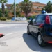Auto dei carabinieri parcheggiata vicino al cartello di ingresso a Pozzallo, con palme e edifici sullo sfondo