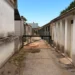 Viale del maneggio comunale tra edifici bassi con porte verdi, una sbarra e cartelli toilette; intonaci ammalorati