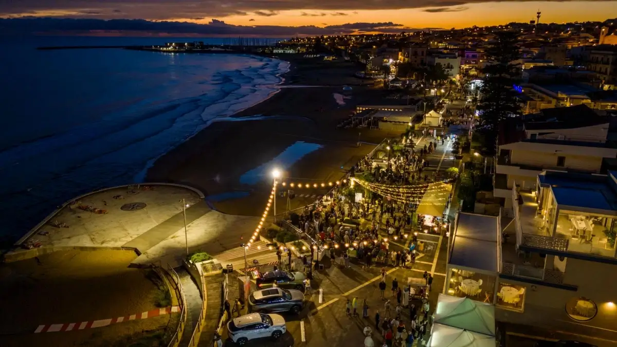 Veduta aerea al tramonto del lungomare di Marina di Ragusa affollato durante Marina Gourmet, tra luci e bancarelle