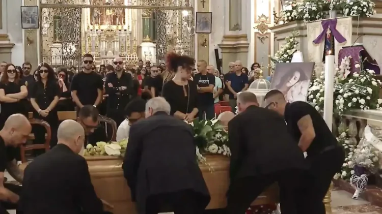 Portatori sollevano il feretro di Michela Canto nella Basilica di Ispica, accanto al suo ritratto tra fiori bianchi