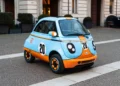 Microlino 777 Collection azzurra e arancione con numero 20 e loghi Gulf, ferma su una strada in pavé davanti a un palazzo