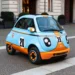 Microlino 777 Collection azzurra e arancione con numero 20 e loghi Gulf, ferma su una strada in pavé davanti a un palazzo