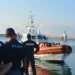 Agenti di Polizia in banchina davanti a una motovedetta della Guardia costiera con migranti a bordo, porto di Pozzallo