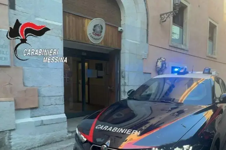 Auto dei carabinieri con i lampeggianti accesi davanti all'ingresso di una caserma dell'Arma, con lo stemma sopra la porta