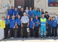 Volontari della Misericordia di Modica in polo blu davanti all'ingresso della sede, con un sacerdote al centro