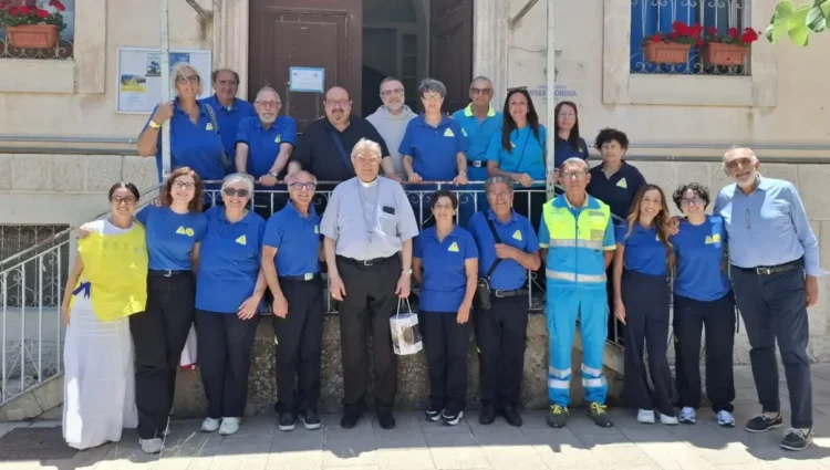Volontari della Misericordia di Modica in polo blu davanti all'ingresso della sede, con un sacerdote al centro