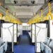 Interno di un autobus urbano con sedili, corridoio centrale e maniglie gialle per i passeggeri