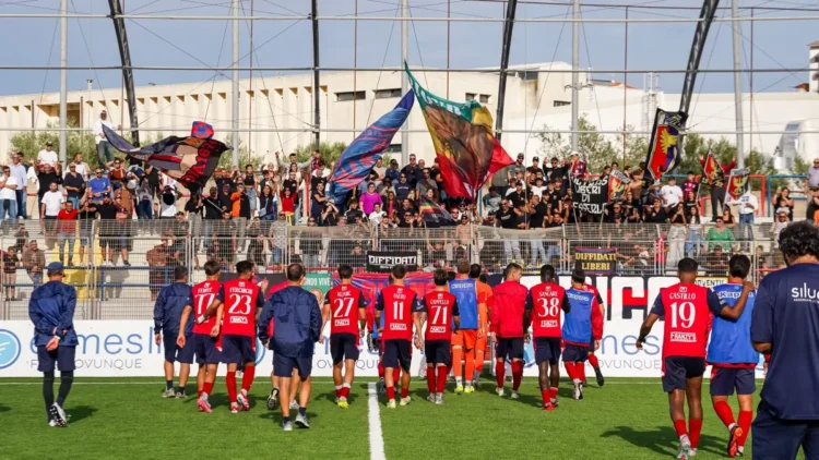 Giocatori del Modica in maglia rossa salutano i tifosi che agitano bandiere in tribuna dopo la gara con il Castrum Favara