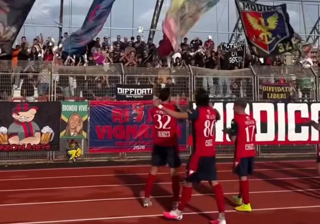 Giocatori del Modica in maglia rossa salutano i tifosi sugli spalti dopo la gara con il Favara Castrum, tra striscioni