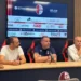Tavolo della conferenza stampa del Modica Calcio, con logo del club e sponsor sullo schermo alle spalle di tre uomini seduti