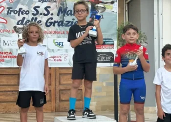 Un giovane ciclista della Motyka Bike School alza il trofeo al centro del podio, tra altri due atleti