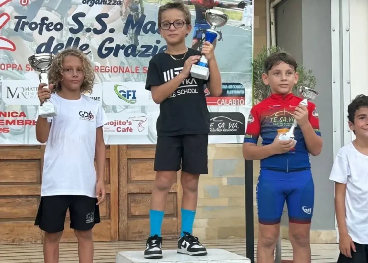 Un giovane ciclista della Motyka Bike School alza il trofeo al centro del podio, tra altri due atleti