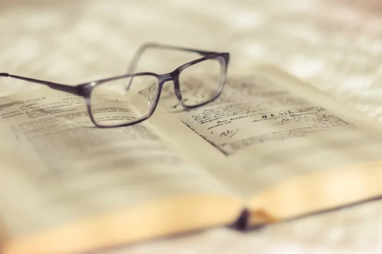 Occhiali da vista appoggiati su un libro antico aperto, con pagine ingiallite e annotazioni scritte a mano