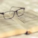 Occhiali da vista appoggiati su un libro antico aperto, con pagine ingiallite e annotazioni scritte a mano