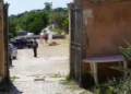 Un carabiniere presidia un cancello con auto dei Carabinieri e persone sfocate dietro il nastro di transennamento