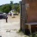 Un carabiniere presidia un cancello con auto dei Carabinieri e persone sfocate dietro il nastro di transennamento