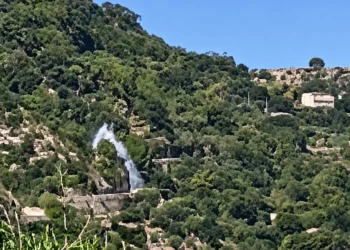 Getto d'acqua che sgorga da una condotta tra la vegetazione sulla collina, con antico muro in pietra sullo sfondo