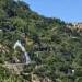 Getto d'acqua che sgorga da una condotta tra la vegetazione sulla collina, con antico muro in pietra sullo sfondo