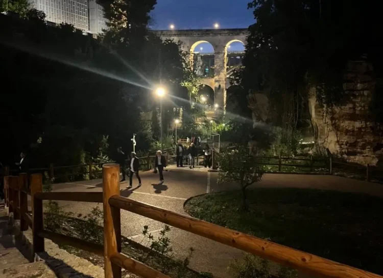 Vialetti illuminati del Parco degli Iblei a Ragusa, nella vallata Santa Domenica, con persone a passeggio e il ponte ad arcate