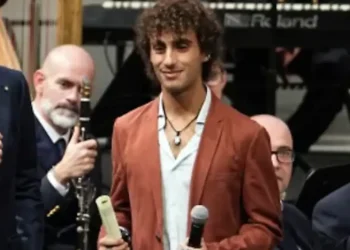 Davide Simone Cavallo sul palco con la pergamena da poliziotto ad honorem, tra due uomini che parlano al microfono