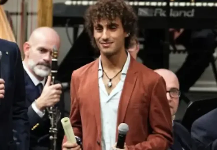 Davide Simone Cavallo sul palco con la pergamena da poliziotto ad honorem, tra due uomini che parlano al microfono