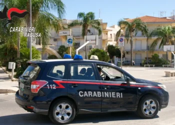 Auto dei carabinieri di Ragusa in transito in una piazza con palme, tra abitazioni e cartelli stradali