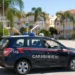 Auto dei carabinieri di Ragusa in transito in una piazza con palme, tra abitazioni e cartelli stradali