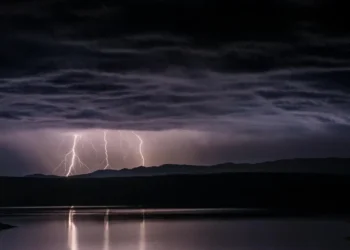 Temporale notturno con fulmini su una catena montuosa, riflesso in uno specchio d'acqua