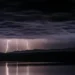 Temporale notturno con fulmini su una catena montuosa, riflesso in uno specchio d'acqua