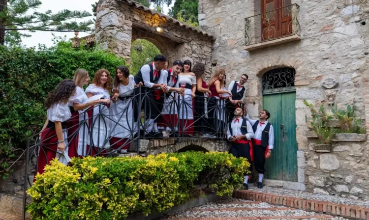Gruppo folk in costume tradizionale siciliano su una scala di un antico edificio in pietra, per la sagra della vendemmia
