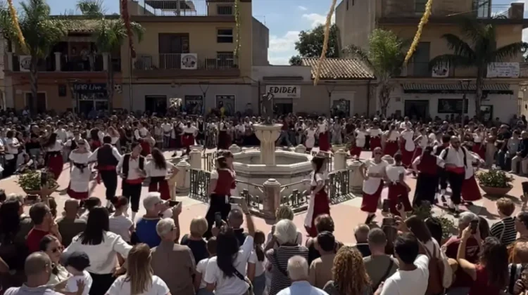 Gruppo folk in costume rosso e bianco balla attorno alla fontana della piazza di Pedalino durante la sagra della vendemmia