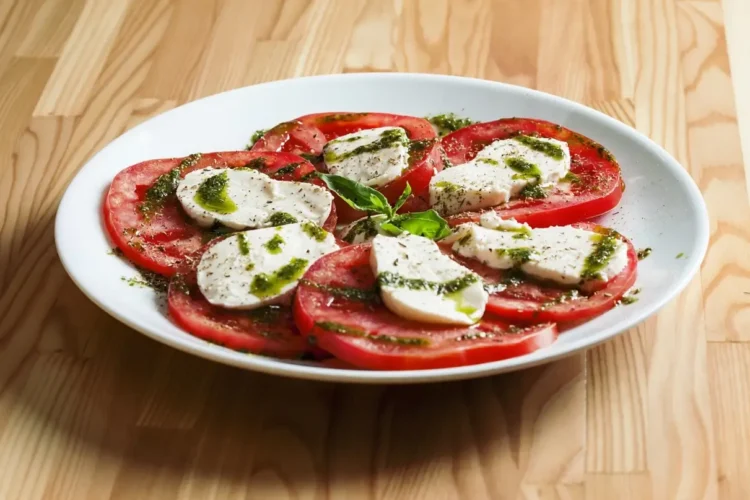 Pomodori a fette con mozzarella, pesto e basilico in un piatto bianco. Immagine generata con intelligenza artificiale